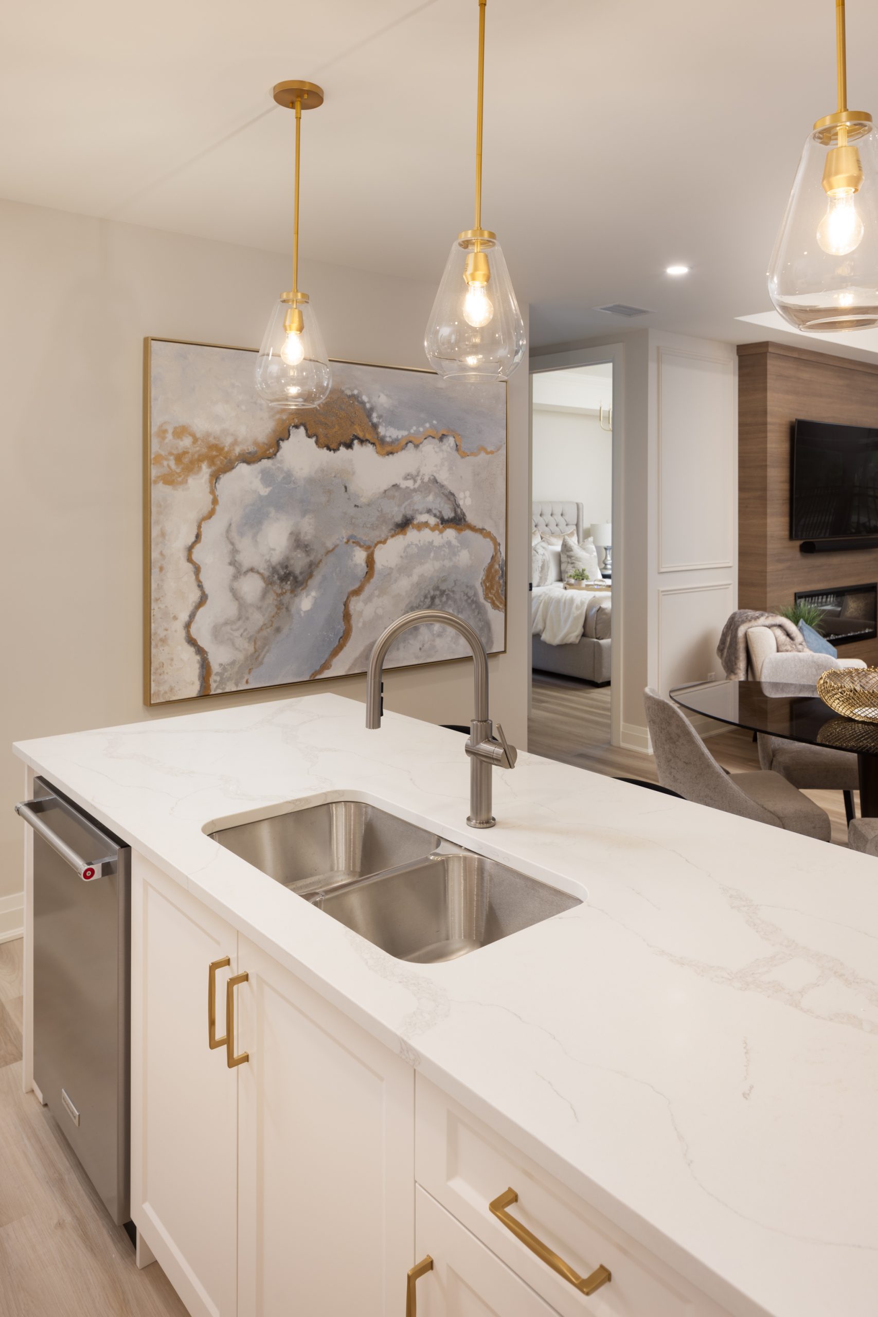 View over the kitchen island into the master bedroom. Kitchen features cream cabinets, white marbled granite counters and gold fixtures.